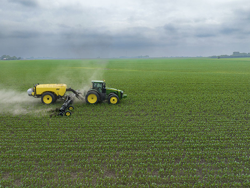 A tractor spreading artificial fertiliser on a corn field